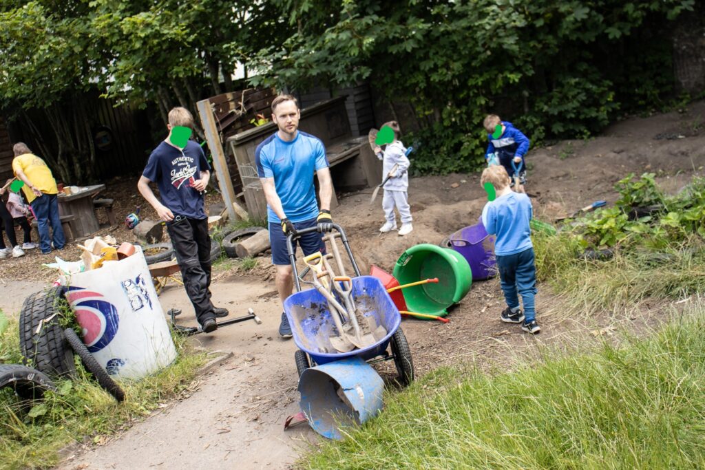 Ryan pushing a wheelbarrow during a playsession of children in the digging pit.